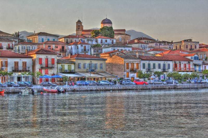 Stone houses with terracotta roofs reflected in the water along the Galaxidi waterfront at dusk